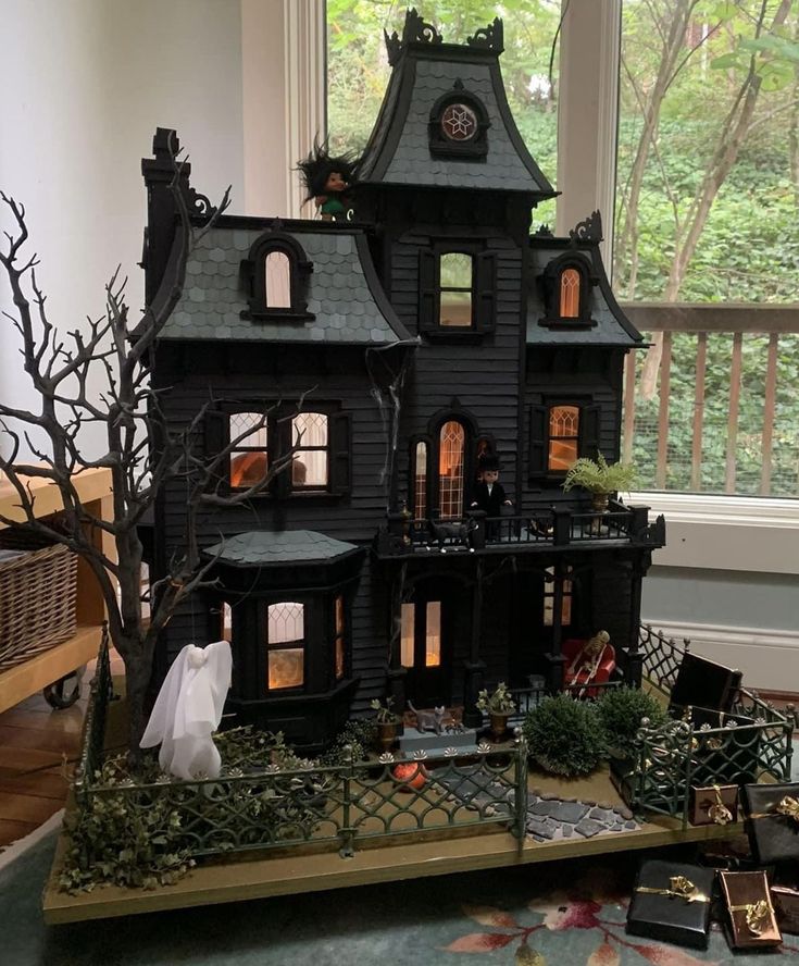 a black doll house sitting on top of a wooden table next to a large window