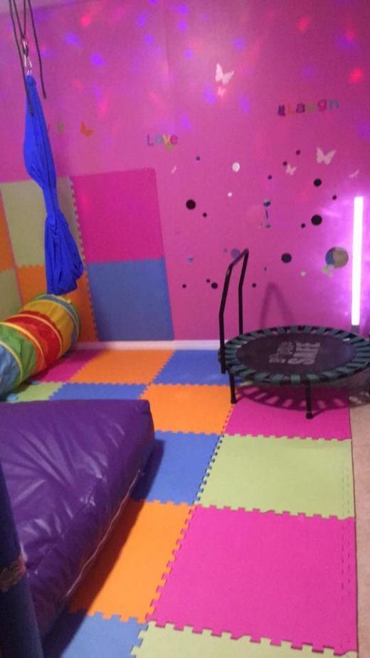 a play room with pink walls and purple flooring, black trampoline in the middle