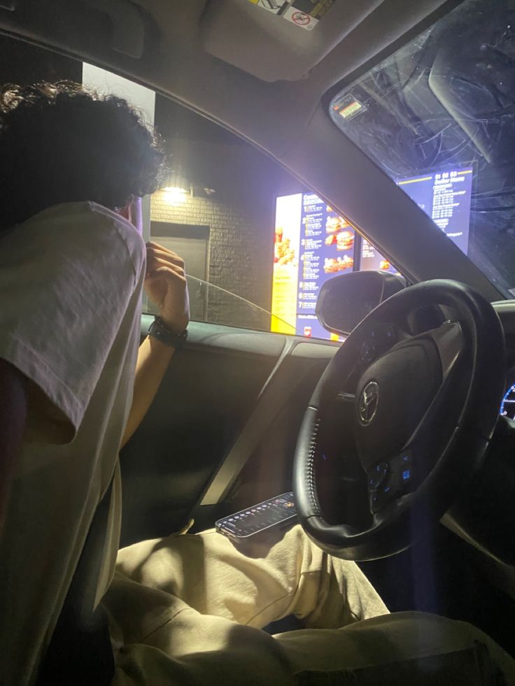 a man sitting in the driver's seat of a car with his hand on the steering wheel