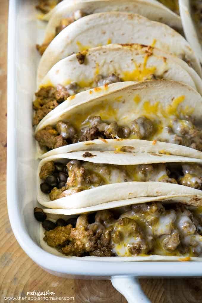 several tacos in a white casserole dish on a wooden table