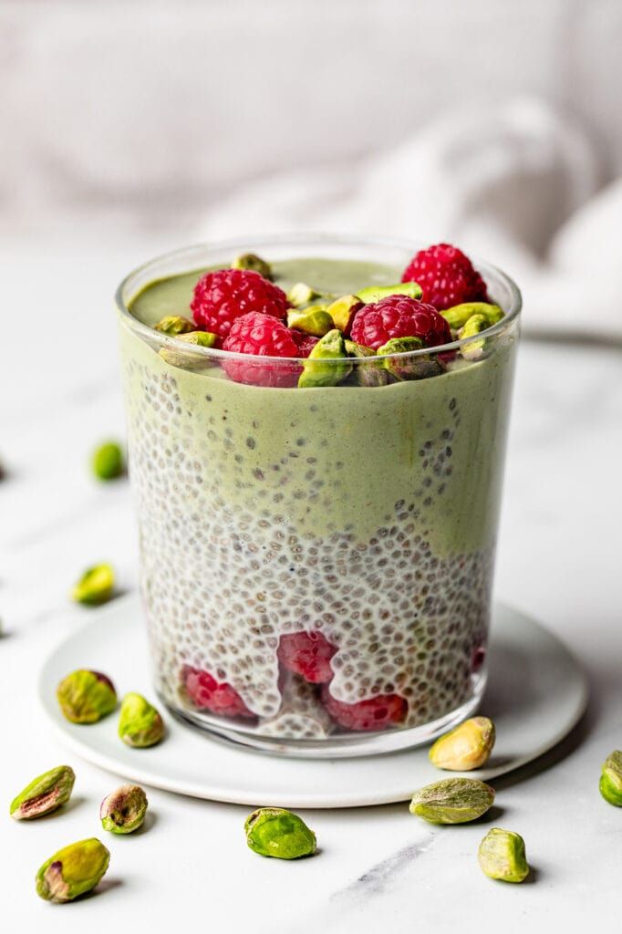 a dessert with raspberries and pistachios in a glass on a plate