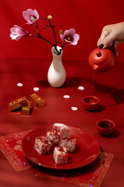 a person pouring tea into a red plate with desserts and flowers in the background