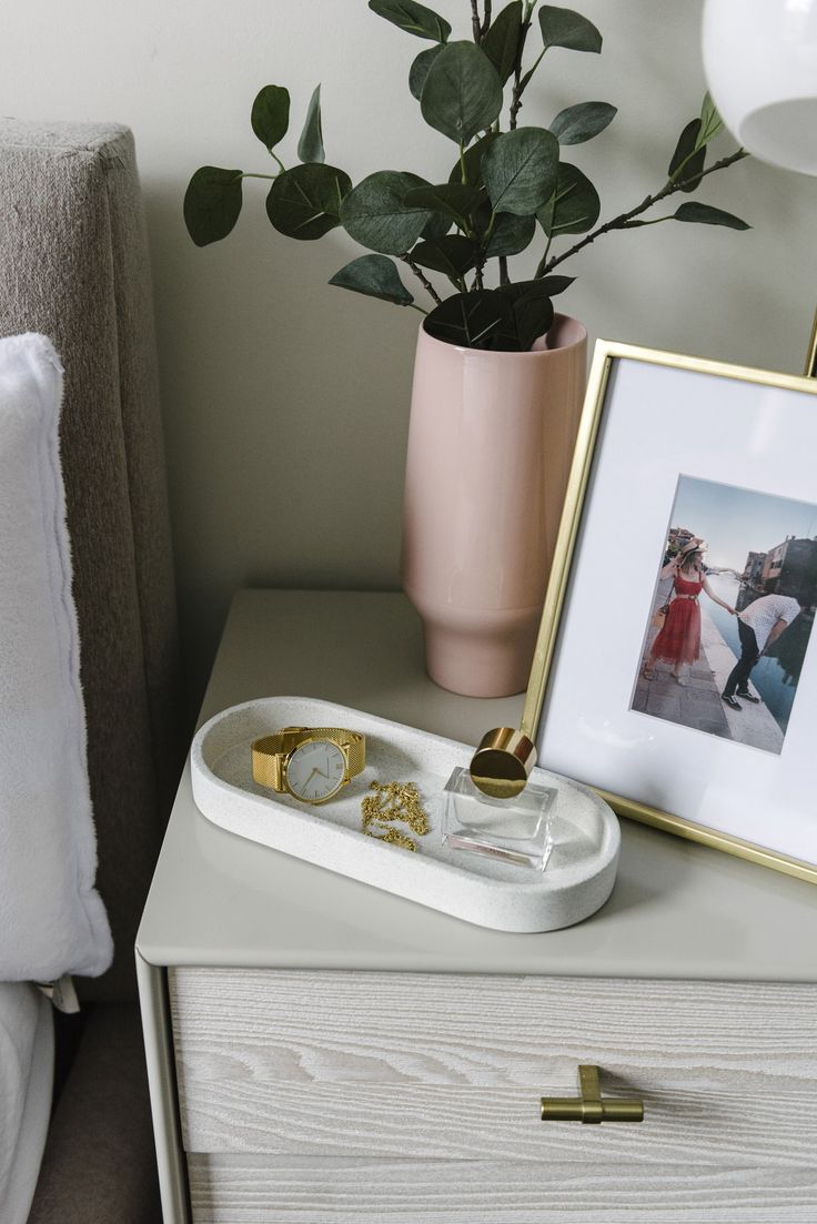 a white dresser topped with a vase filled with flowers next to a framed photo and two gold rings