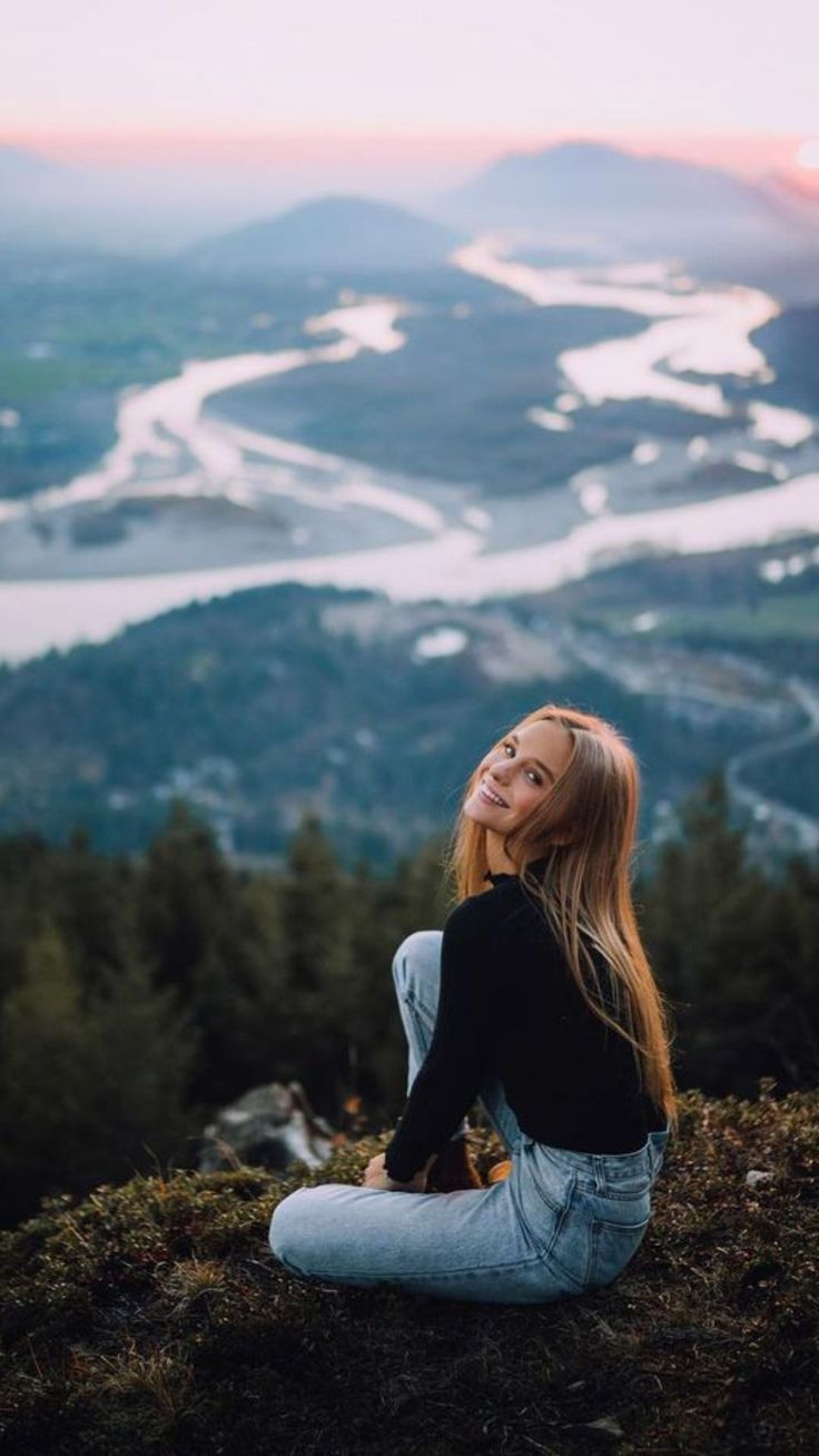 a woman sitting on top of a hill looking at the sky