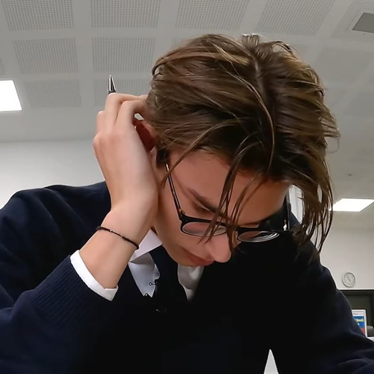 a young man with glasses is holding his head to his ear while looking at something