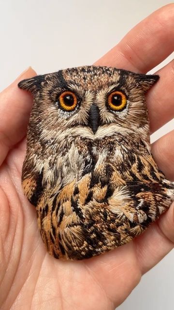 a hand holding an owl shaped rock in it's left hand, with orange eyes