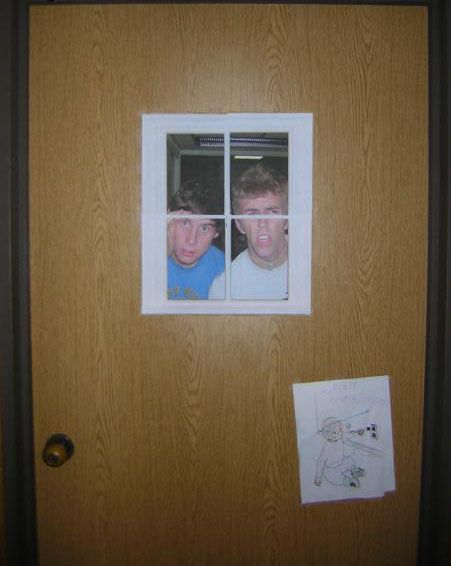 two young boys looking through the window of a wooden door with paper taped to them