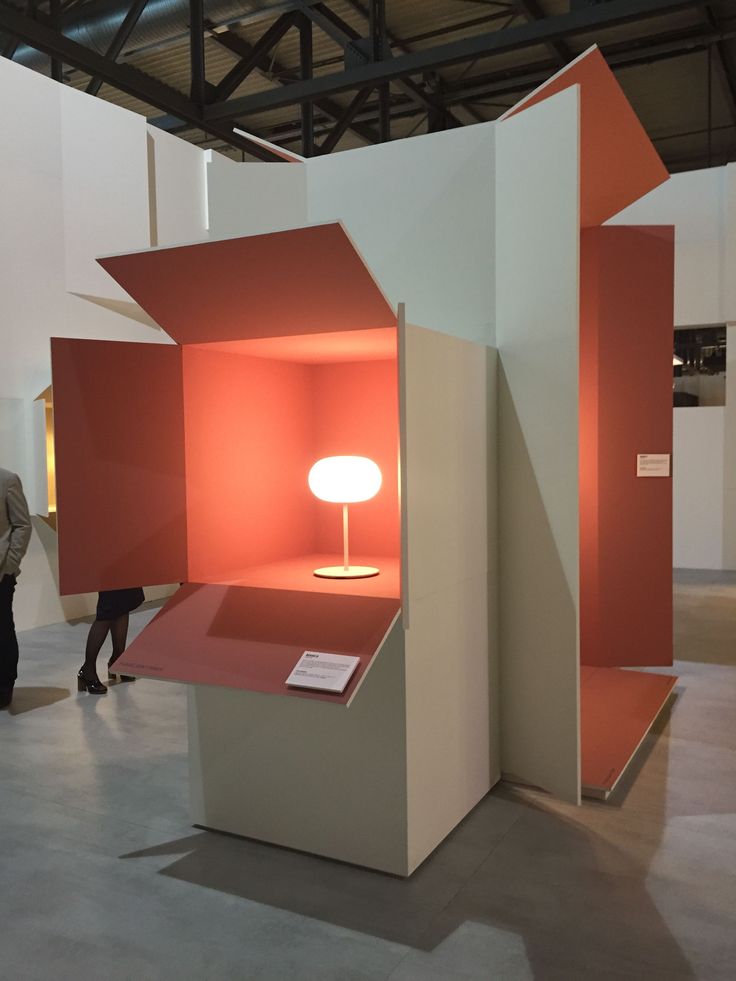 people are looking at an orange and white display in a room with two lamps on the floor