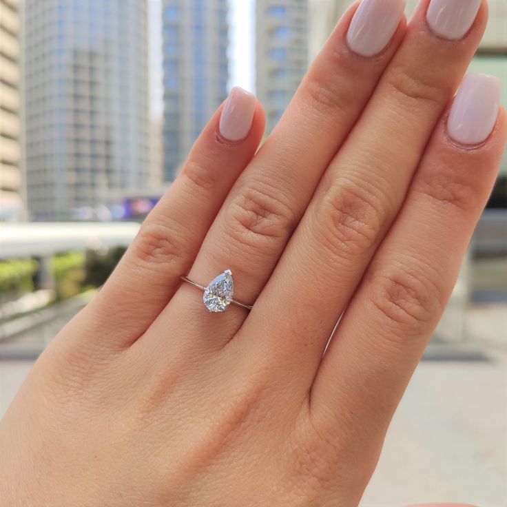 a woman's hand with a diamond ring on top of her finger and buildings in the background