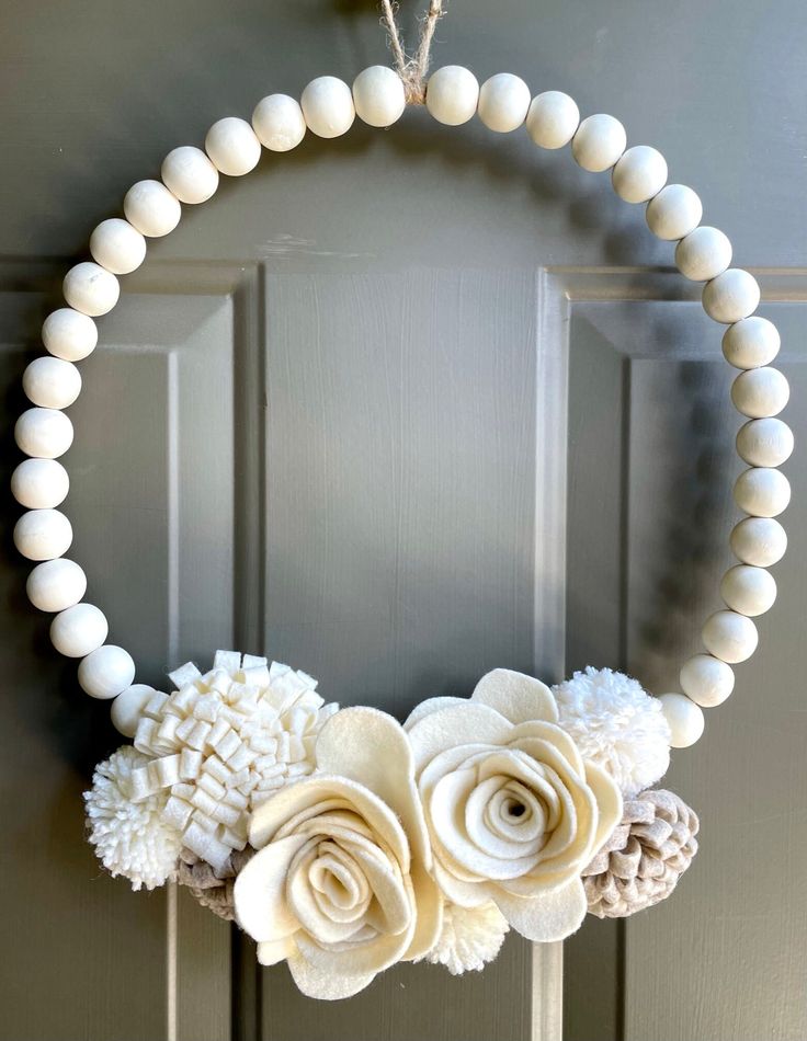 a white wreath with flowers and beads hanging on a front door hanger in the shape of a circle