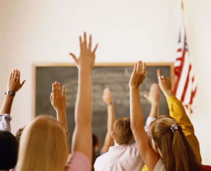 several children raising their hands in front of a chalkboard with an american flag on it