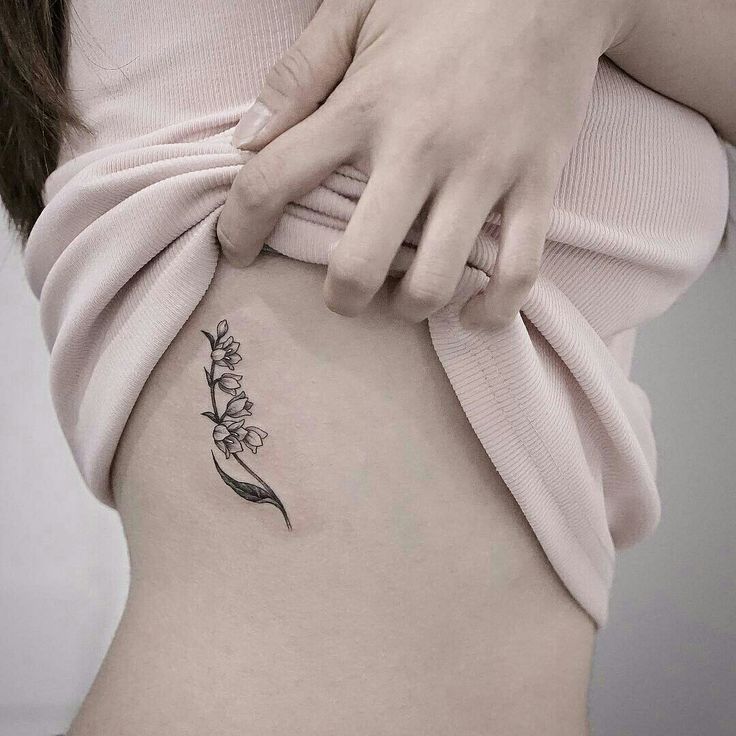 a woman's stomach with a small flower tattoo on her side ribcage