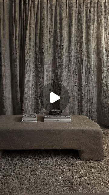 a couch sitting in front of a curtain next to a table with books on it