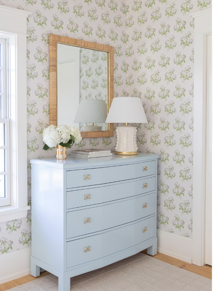 a blue dresser with flowers on it and a mirror in the corner next to it