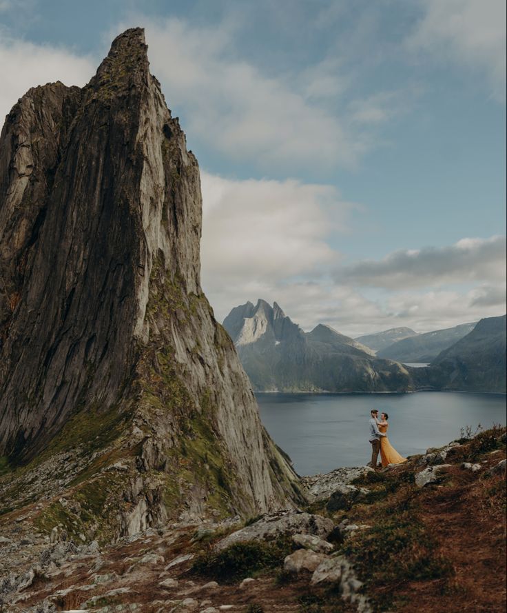 a couple standing on top of a mountain next to a lake