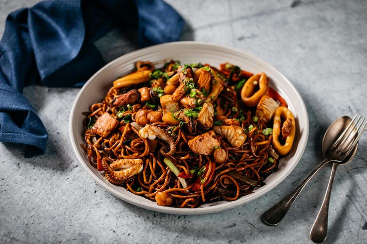 a white bowl filled with noodles and meat on top of a table next to silverware