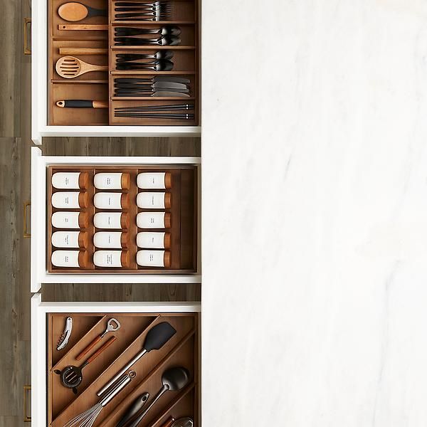 an open drawer with utensils and spoons in it on top of a white wall