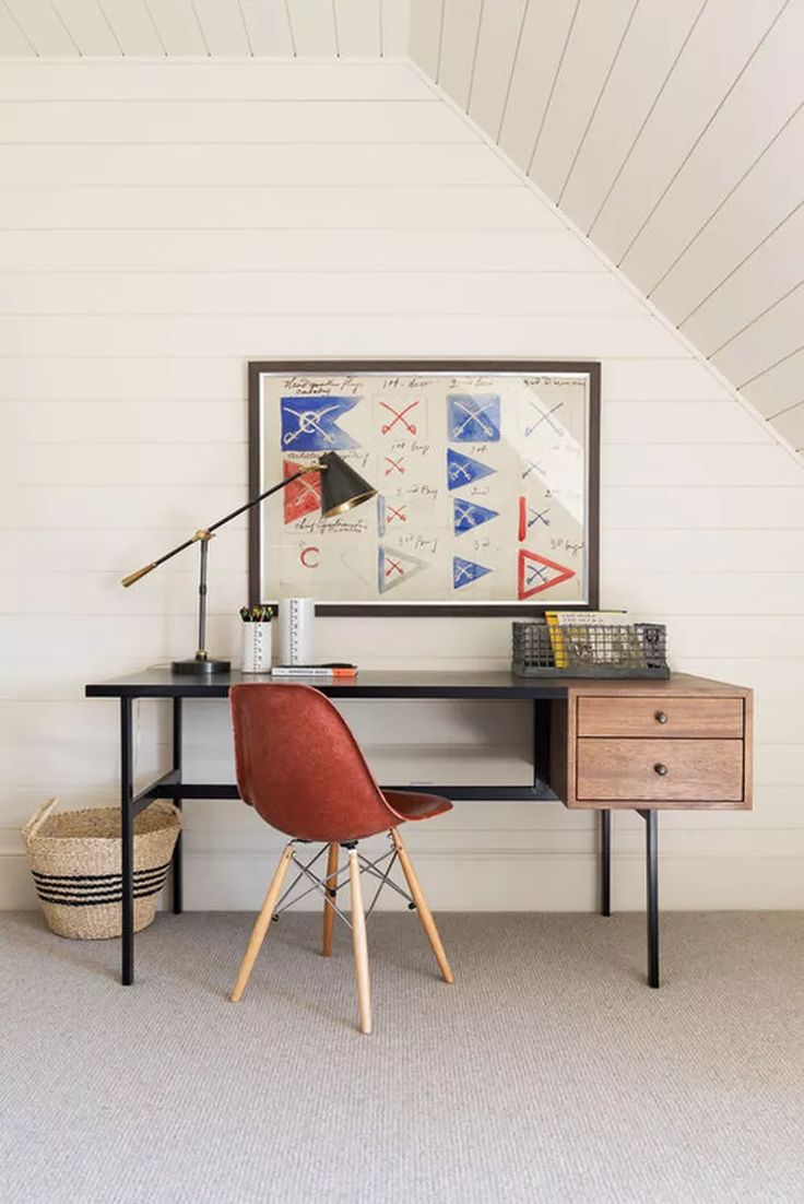 a desk with a chair, lamp and pictures on the wall above it in a white room