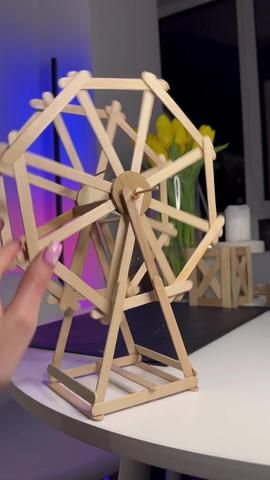 a wooden model of a ferris wheel being held up by someone's hand on a table