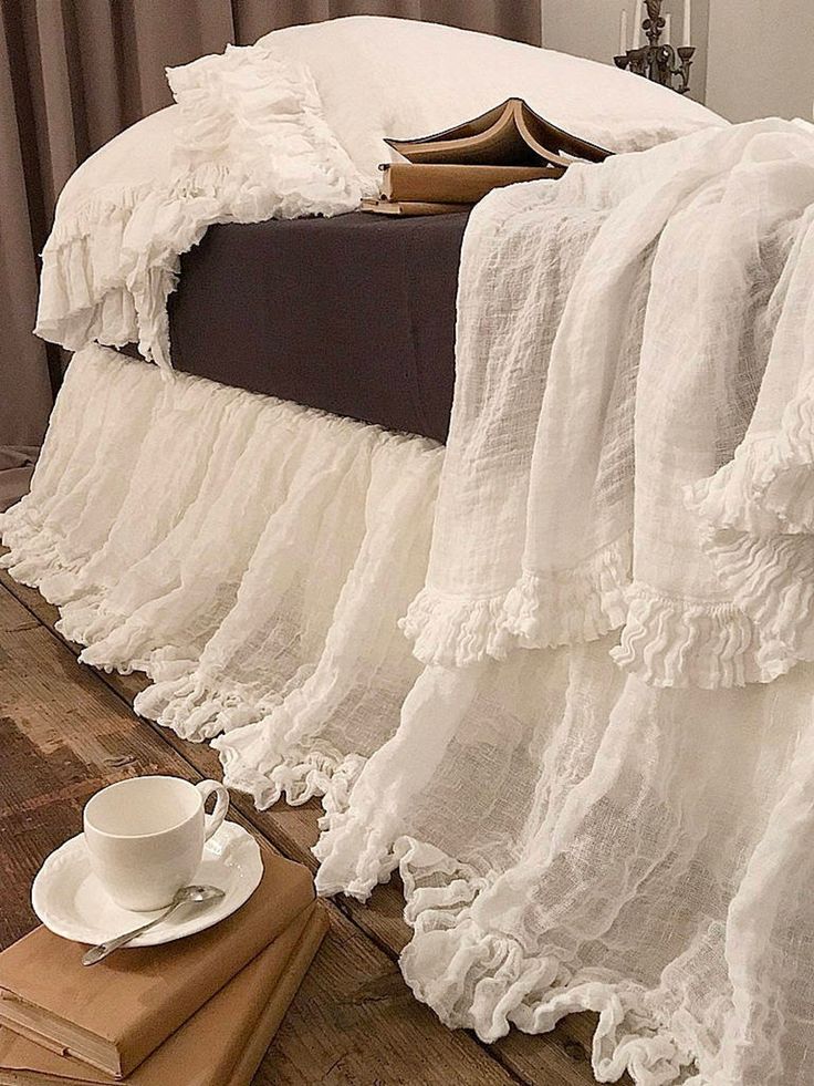 a white bed with ruffled bedspread and coffee cup on the floor next to it