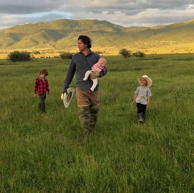 a man holding a baby while walking in a field with two other people behind him