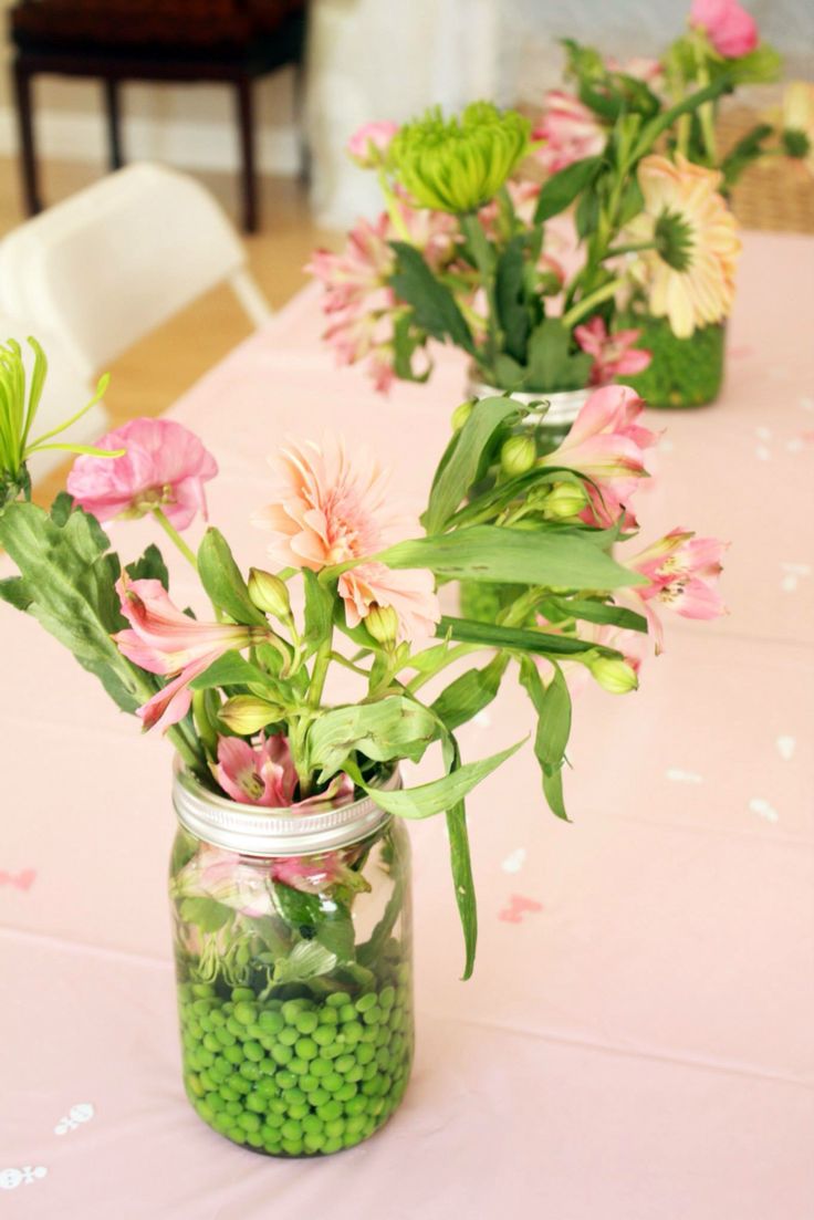 three mason jars filled with flowers sitting on top of a pink tablecloth covered table