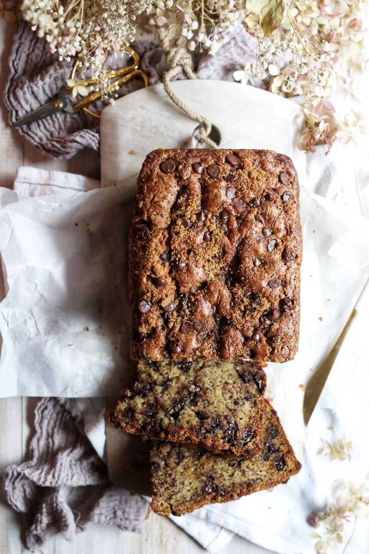 two slices of chocolate chip banana bread sitting on top of white napkins next to dried flowers