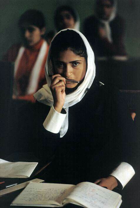 a woman sitting at a desk in front of papers and holding a pen to her mouth