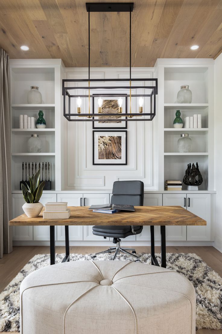 a desk with a chair and ottoman in front of white bookcases under a wooden ceiling