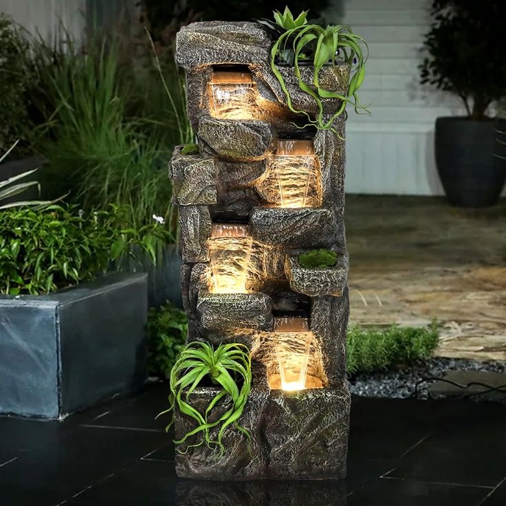 an outdoor fountain made out of rocks with plants growing on it and lit candles in the center