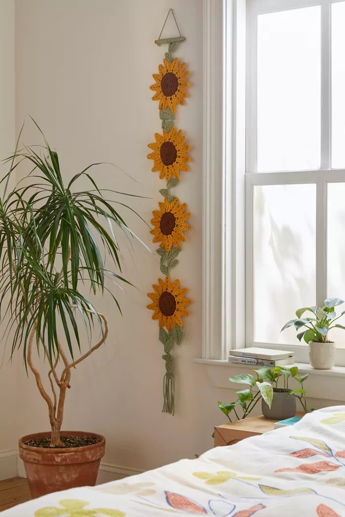 a sunflower wall hanging next to a potted plant in front of a window