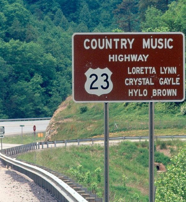 a highway sign on the side of a road in front of some trees and bushes