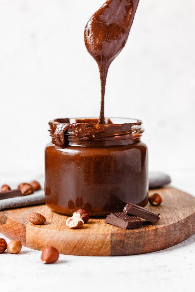 a spoon full of chocolate spread on top of a jar with almonds around it