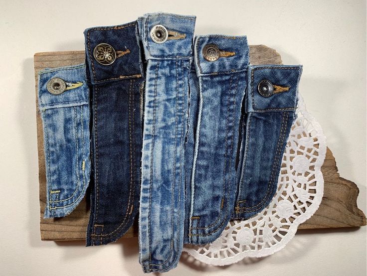 four pairs of jeans are hanging on a wooden board with lace doily around them