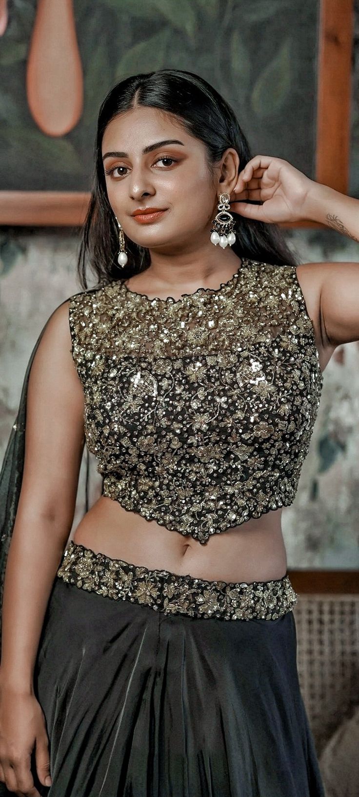 a woman in a black and gold dress with her hands on her head, posing for the camera