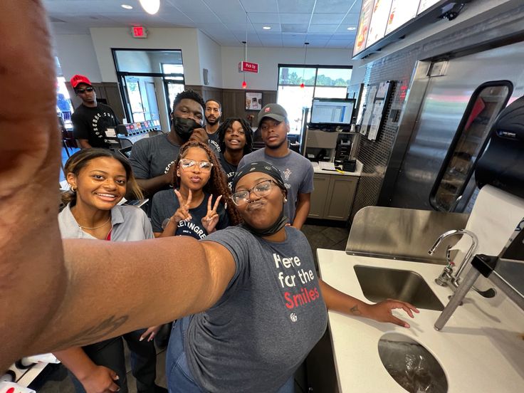 a group of people taking a selfie in a kitchen with stainless steel appliances and counters