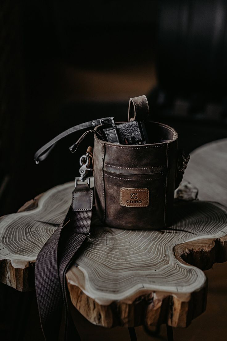 a brown leather bag sitting on top of a wooden table next to a tree stump