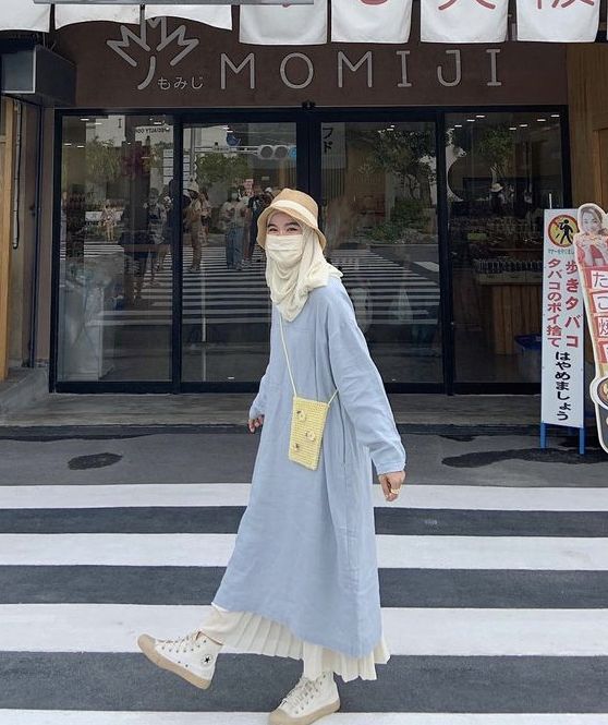 a woman walking across a cross walk in front of a momu store wearing a face mask