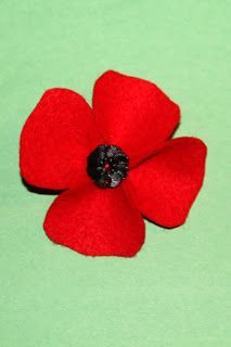 a red felt flower with black center on a green background, ready to be made into brooch