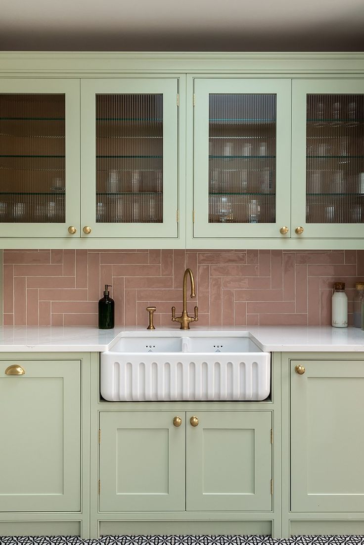 a kitchen with green cabinets and pink tile backsplash, gold faucets