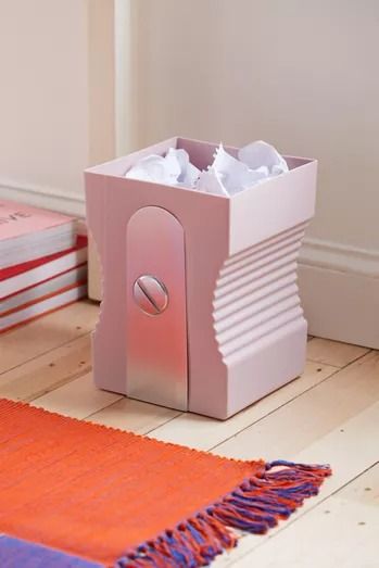 a pink box sitting on top of a wooden floor next to two red and white books