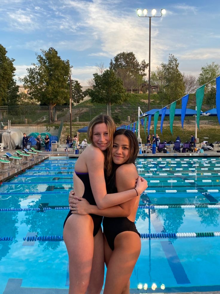 two women in swimsuits hugging each other by the side of a swimming pool