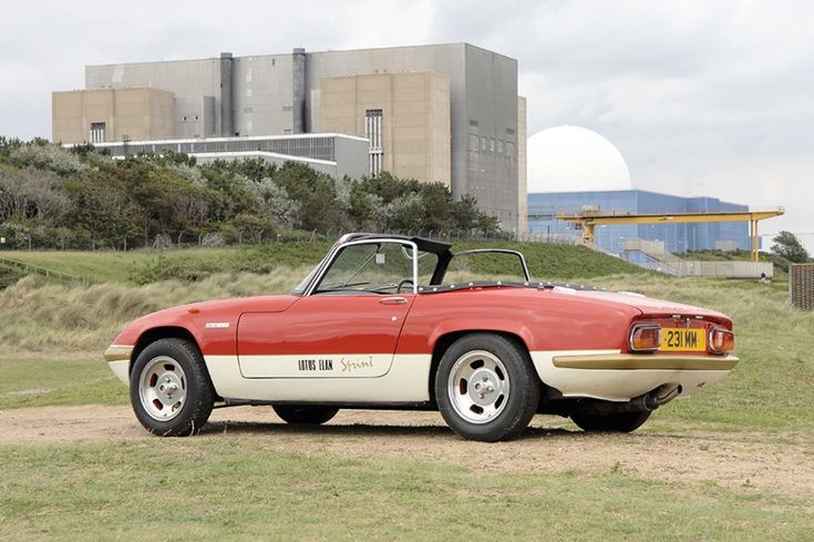 an old red and white sports car parked in front of a large building on a hill