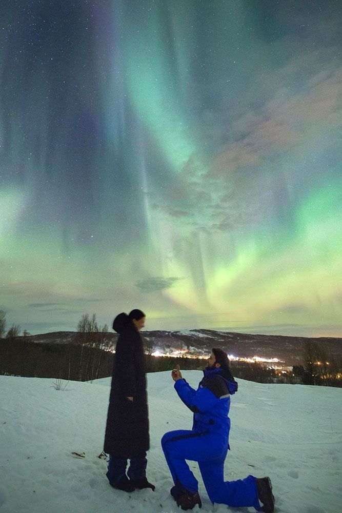 two people are standing in the snow under an auroral sky with green and purple lights