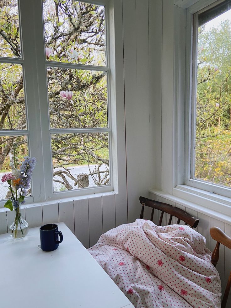 a table and chair in a room with two large windows, one has a blanket on it