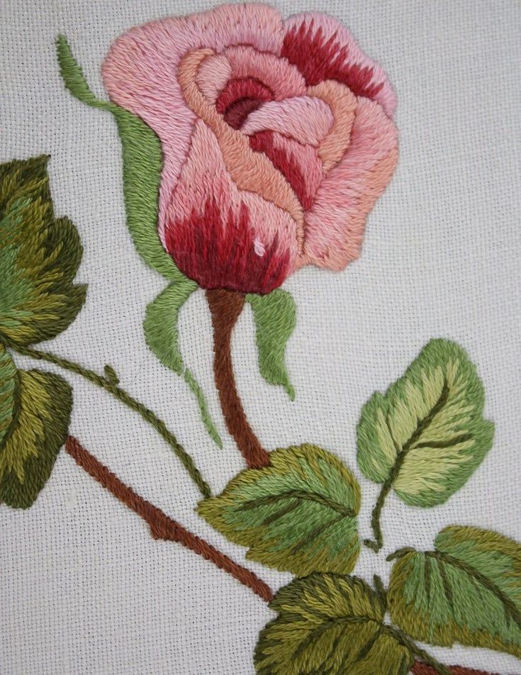 an embroidered rose with green leaves on a white background