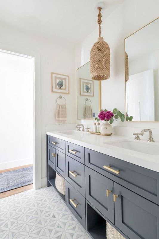 a bathroom with blue cabinets and white counter tops, gold accents on the mirror over the sink