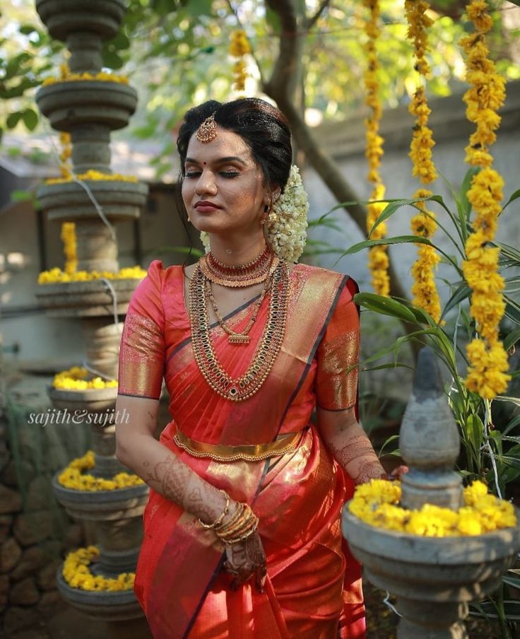 a woman in a red and gold sari standing next to yellow flower garlands