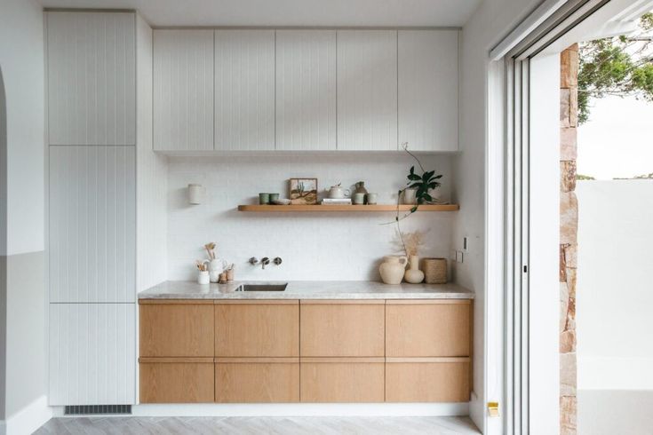 a kitchen with white walls and wooden cabinets next to a sliding glass door that leads outside