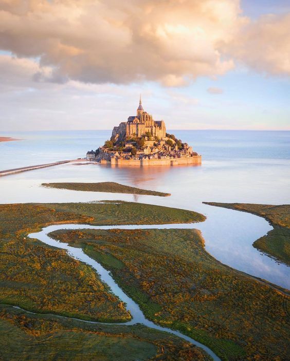 an island in the middle of water with a castle on it's top surrounded by land